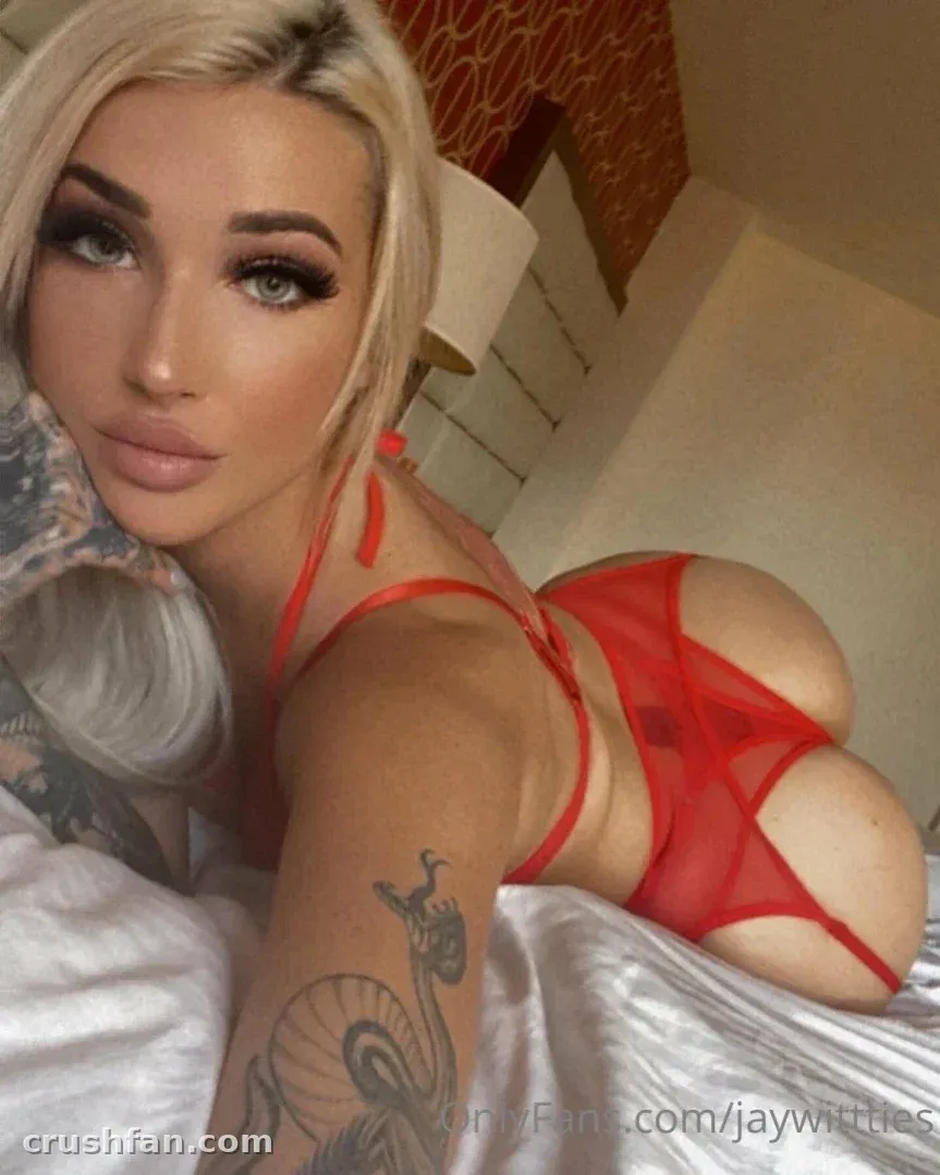 Mulher loira em lingerie vermelha transparente reclinada em lençóis brancos em ambiente interno