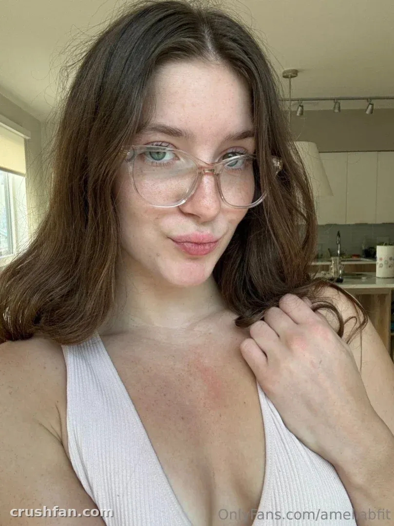 Amelia mit klarer Brille und einem weißen gerippten Tanktop in einer hellen Küche