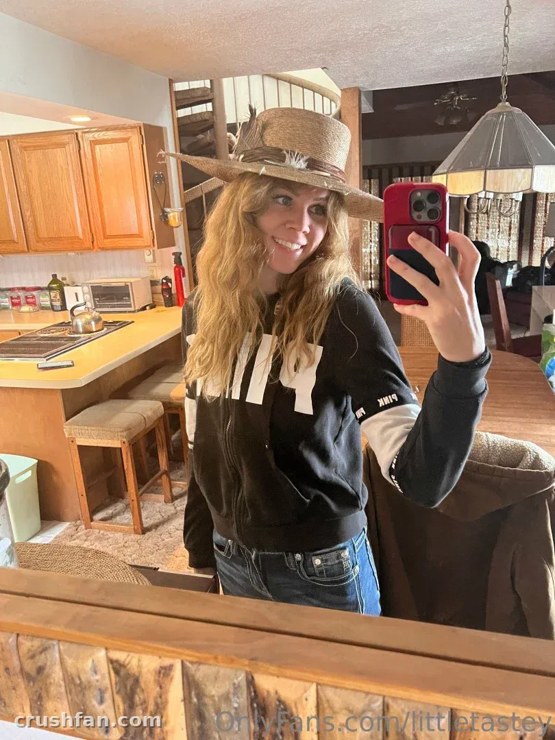 Jaylen in a straw hat taking a mirror selfie in a rustic kitchen with wooden cabinets.