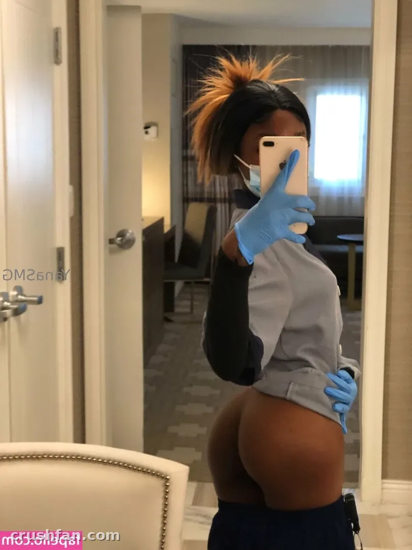 YanaSMG com um top cinza e preto tira uma selfie no espelho em um quarto de hotel.