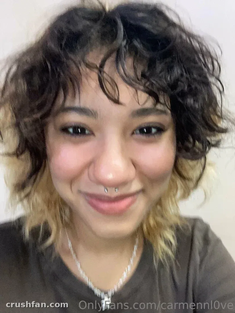 A oficial Carmen Love sorrindo em uma selfie em close-up com cabelo curto ondulado e um colar prateado.