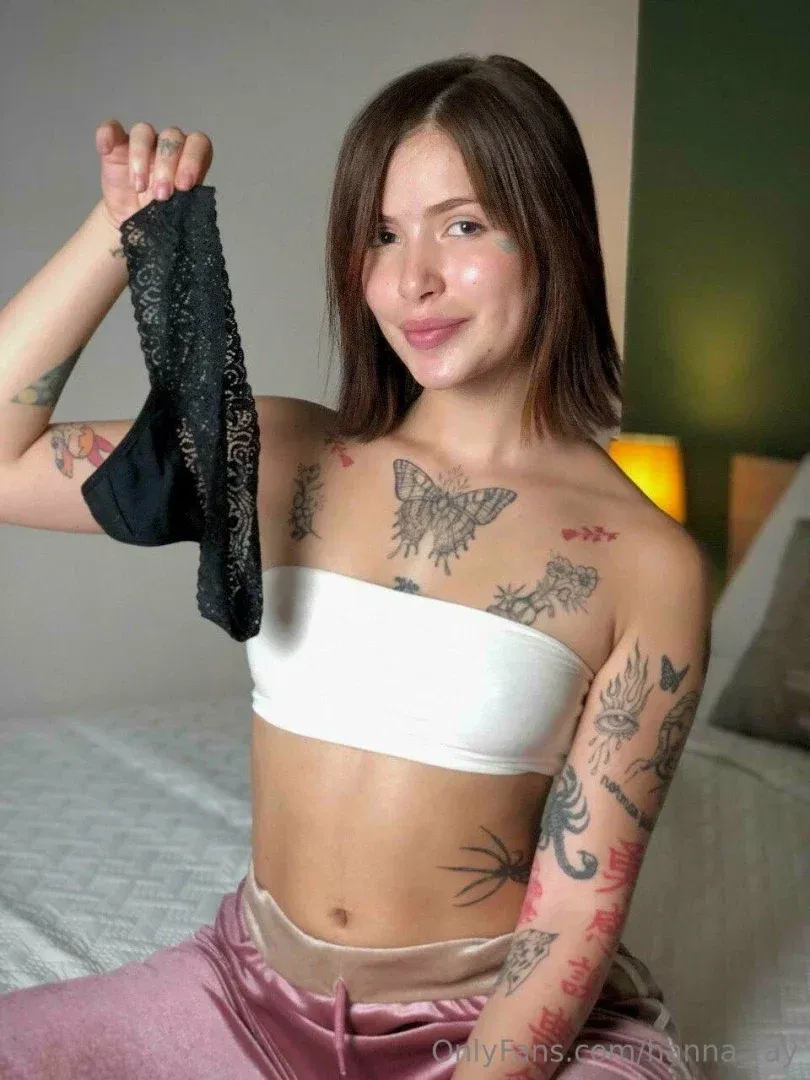 Mulher de bandeau branco e calças de cetim rosa segurando lingerie de renda preta em um quarto