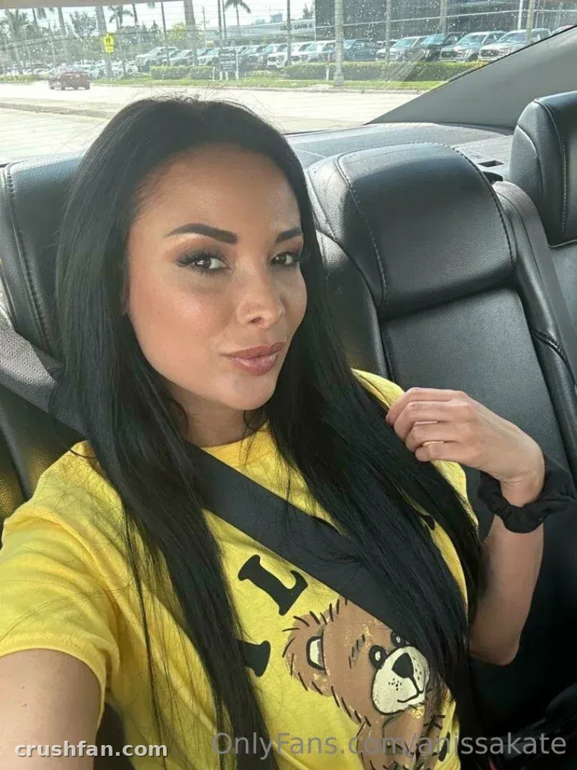 Anissa Kate trägt ein gelbes Grafik-T-Shirt und sitzt in einem Auto mit dunklen Ledersitzen.