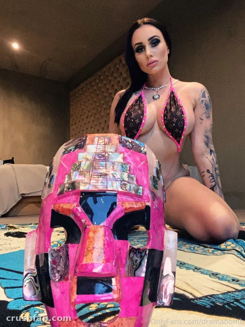 MONEYBIRDETTE VIP kneeling indoors beside a pink mirrored helmet on a patterned rug