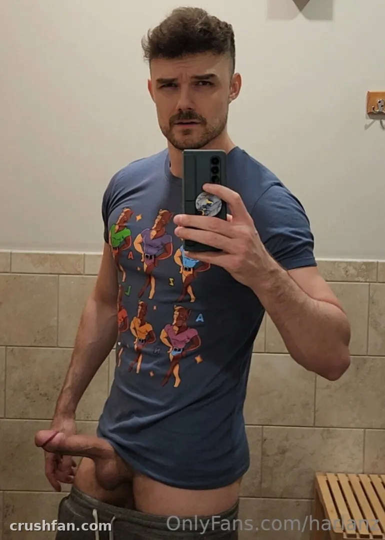 Harlan in a blue graphic tee taking a bathroom mirror selfie.