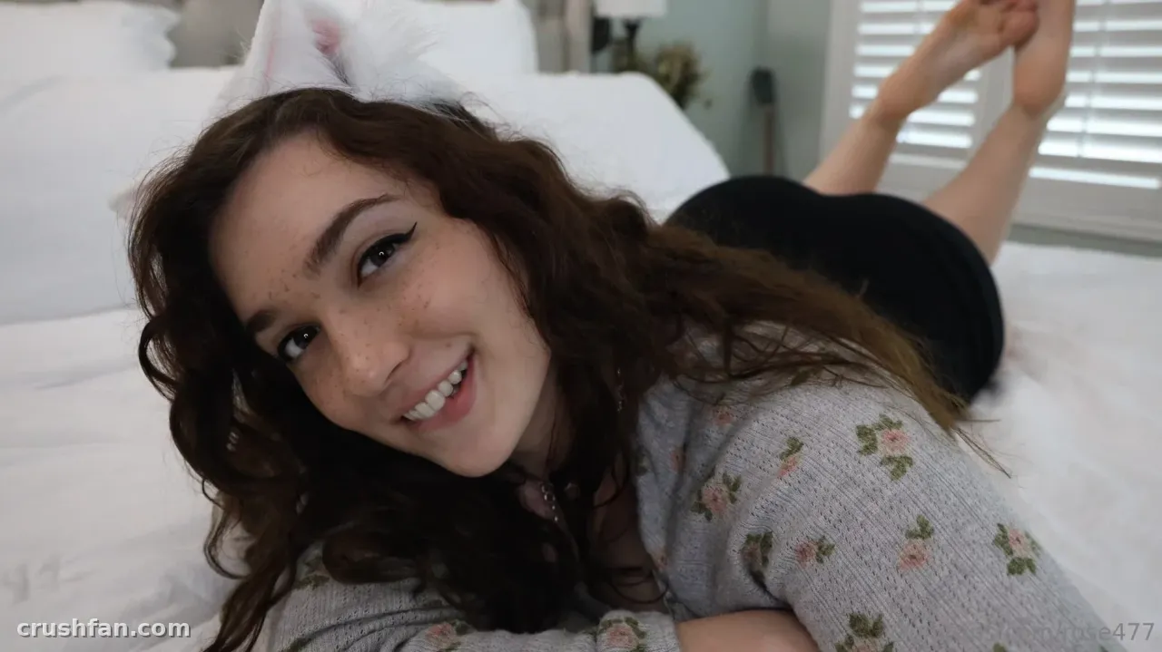 Rose smiling while lying on a white bed in a grey floral cardigan