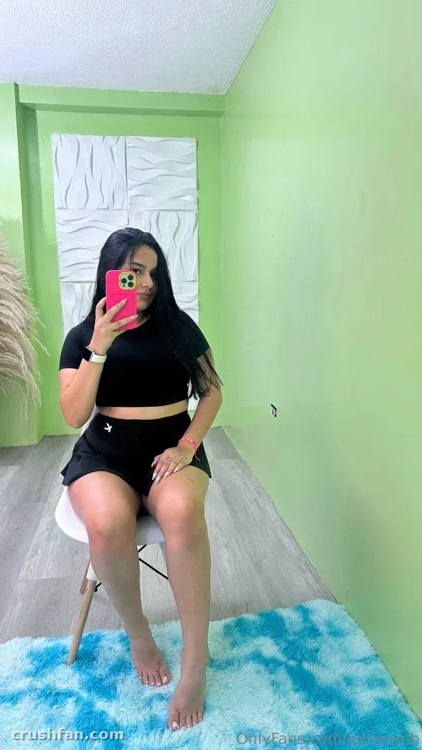 Adripiecitos in einem schwarzen Crop-Top und Shorts macht ein Spiegel-Selfie in einem hellgrünen Raum.