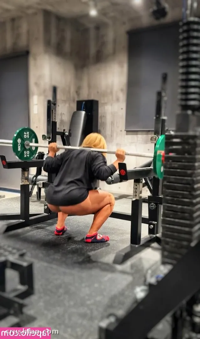 Sakura in a dark top and rust leggings doing a barbell back squat in a concrete gym.