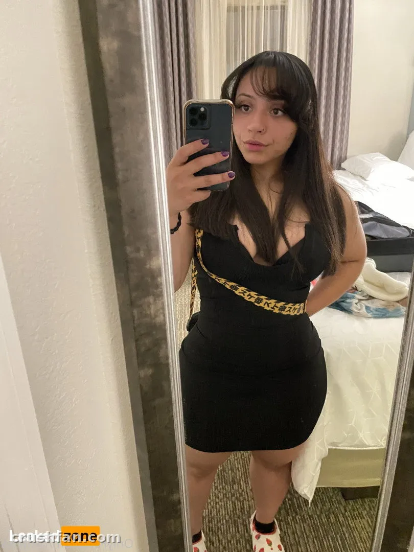 Nixlynka prenant un selfie miroir dans une robe noire avec une ceinture à chaîne dorée.