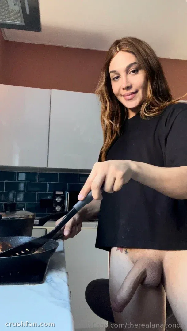 Creator in a black t-shirt holding a spatula over a pan in a kitchen