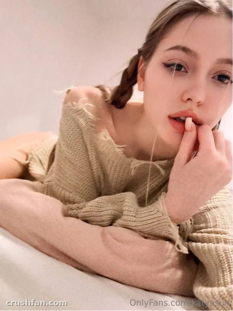 Katya Sun dans un pull en tricot beige avec des cheveux tressés, reposant sur une surface claire