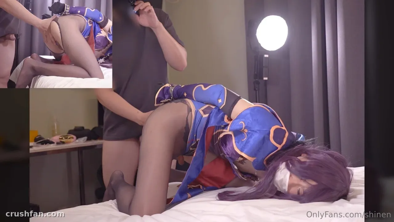 Haru in a blue cosplay outfit on a white bed with a studio light behind.