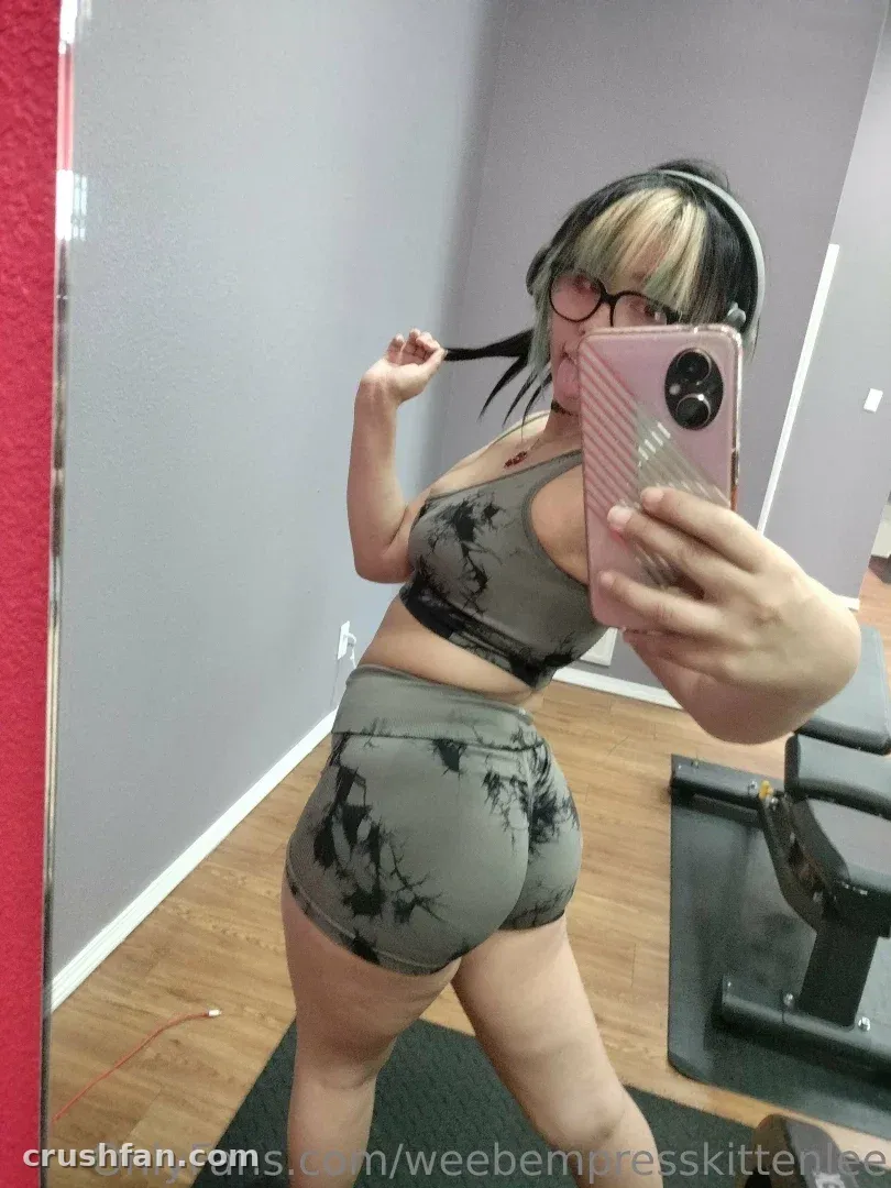 EmpressKoneko macht ein Spiegel-Selfie in einem grauen Batik-Trainingsset in einem Homegym.