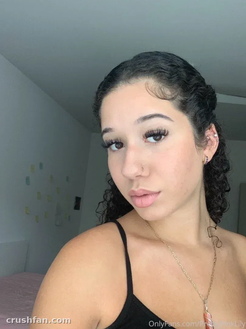 Selfie em close-up de uma mulher de blusa preta com colar dourado em um quarto iluminado.