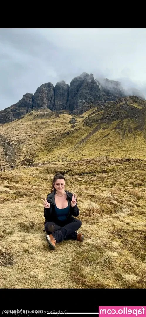 Jade sitting cross-legged on a grassy hillside with misty mountains behind her