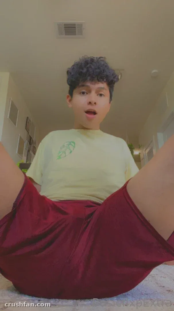 Creator in a pale green tee and red shorts sitting indoors, looking at the camera.