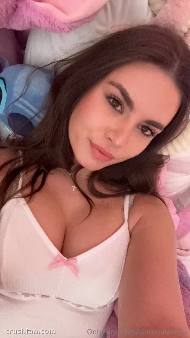 Lauren Alexis takes a close selfie in a white top against pastel pink bedding
