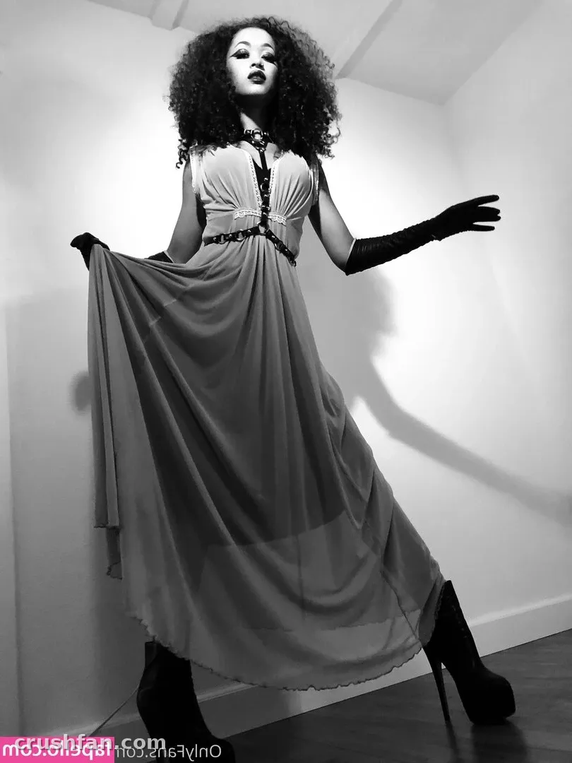 Retrato en blanco y negro de Skin Diamond con un vestido fluido y guantes largos frente a una pared blanca