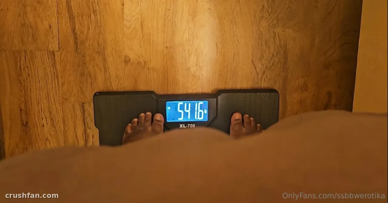 Pieds nus sur une balance numérique avec un écran bleu sur un sol en bois.