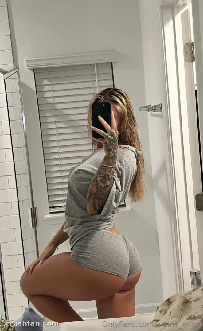 Alaina in grey loungewear taking a mirror selfie in a bright bathroom.
