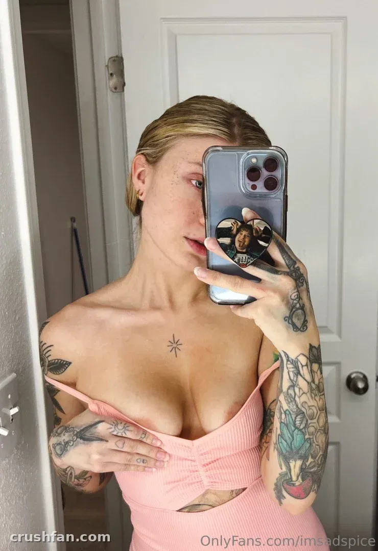 Liz takes a mirror selfie in a pink top in front of a white door.