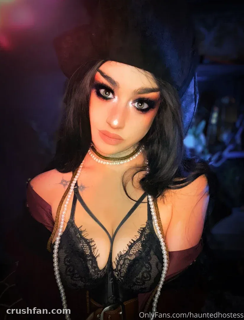 Haley Quinn в чёрном кружевном топе и тёмной шляпе, с жемчужными украшениями при атмосферном освещении.