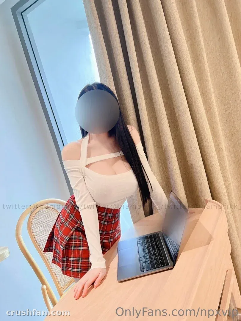 Creator in a white off-shoulder top and red plaid skirt standing by a desk with a laptop.