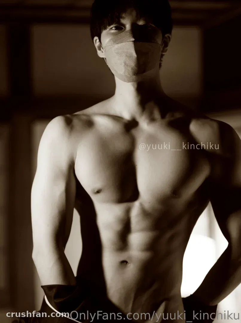 Sepia studio portrait of Yuuki wearing a cloth mask, bare-chested against a blurred backdrop.