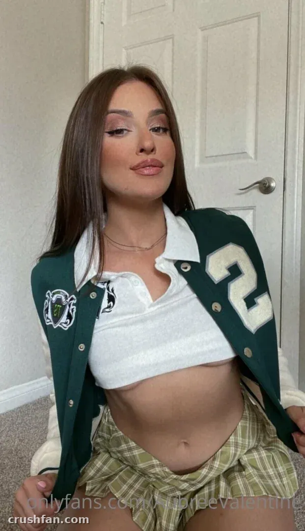 Creator in a green varsity jacket and plaid skirt seated indoors by a white door