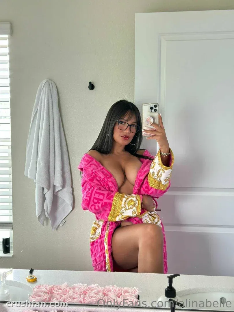 Alina in a pink and gold robe taking a mirror selfie in a bright bathroom