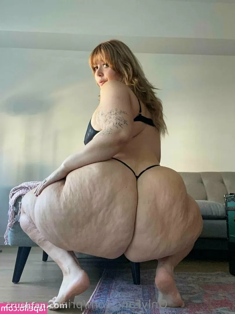 Princess Pear standing in profile in a bright living room wearing dark lingerie