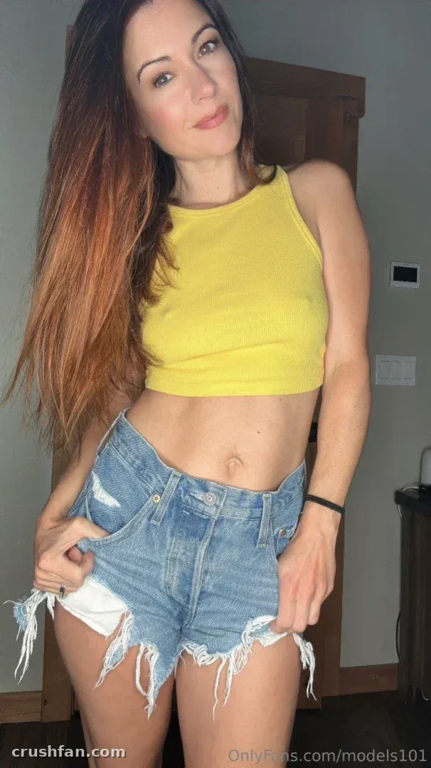 Creatorin in einem gelben Crop-Top und Jeansshorts, drinnen stehend