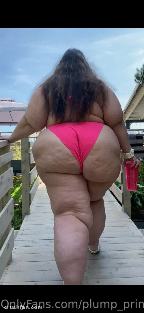 Plump Princess em um maiô rosa em pé em uma passarela de madeira ao ar livre