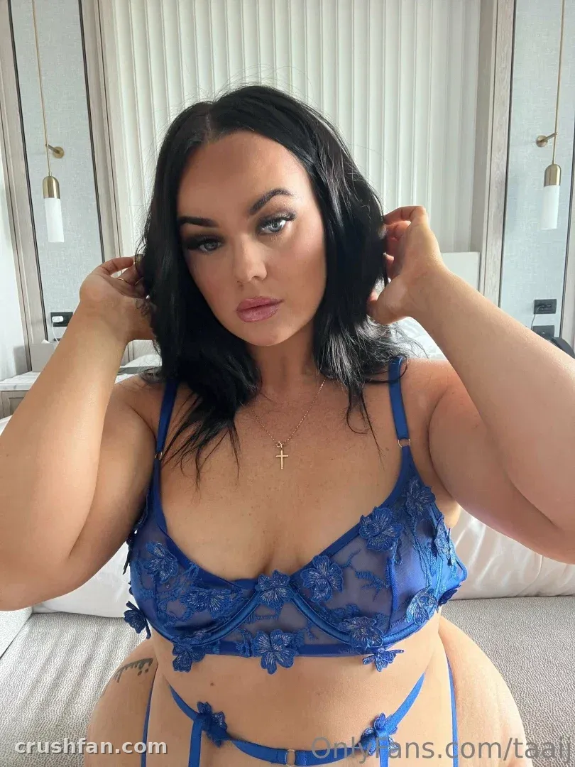 Creator in blue lace lingerie adjusting her hair in a softly lit bedroom selfie