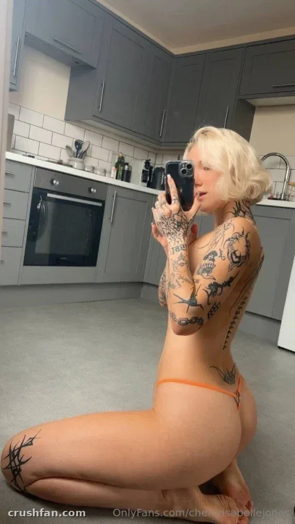 Cherry стоит на коленях на кухонном полу и делает селфи в зеркале, позади неё серые шкафы