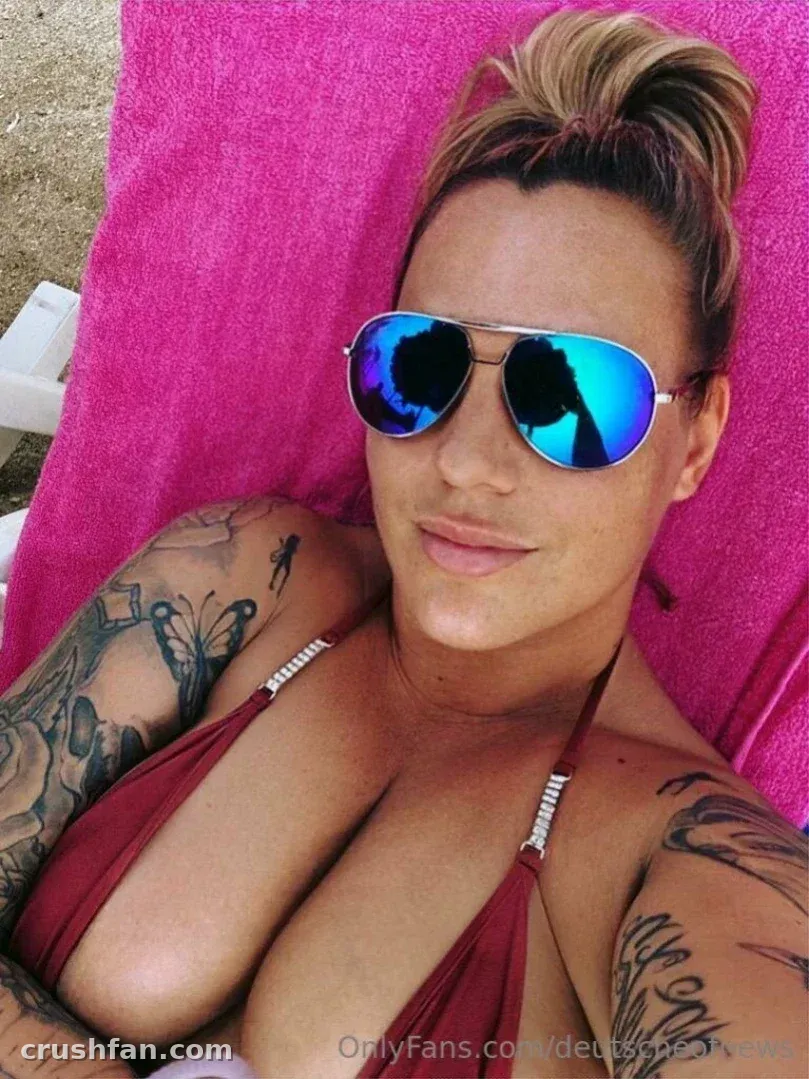 Deutsche Onlyfans in mirrored sunglasses and a red top resting on a pink towel outdoors.