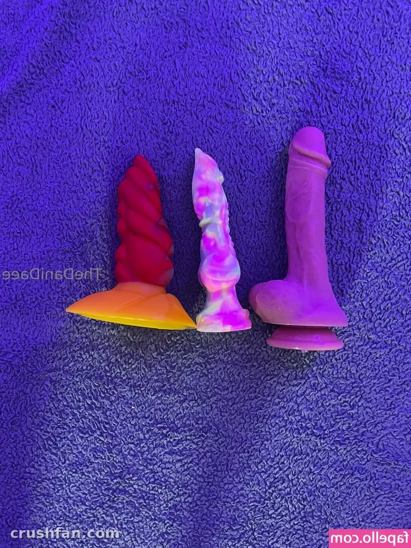 Three colourful silicone toys lined up on a textured purple towel under purple light