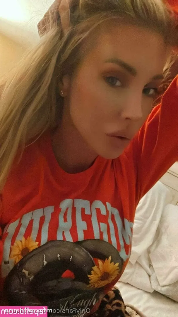 Samantha Saint in an orange graphic T-shirt posing for a close indoor selfie.