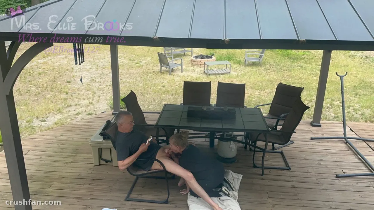 Ellie Brooks sitzt auf einer überdachten Holzterrasse mit Gartenmöbeln und einem grasbewachsenen Hof dahinter