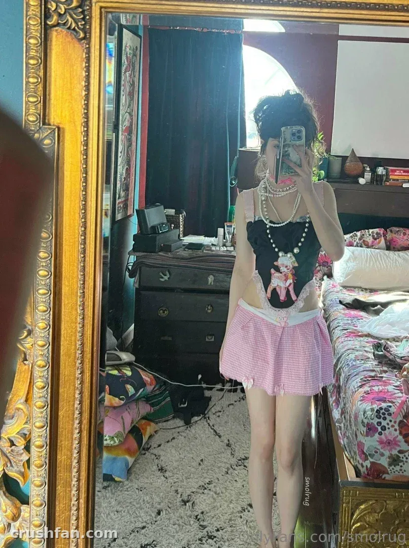 Femme en haut noir et jupe rose à carreaux vichy prenant un selfie dans un miroir au cadre doré ouvragé