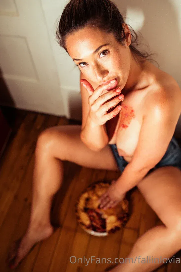 Eva Lovia seated on a wooden floor beside a pie in a casual indoor setting.