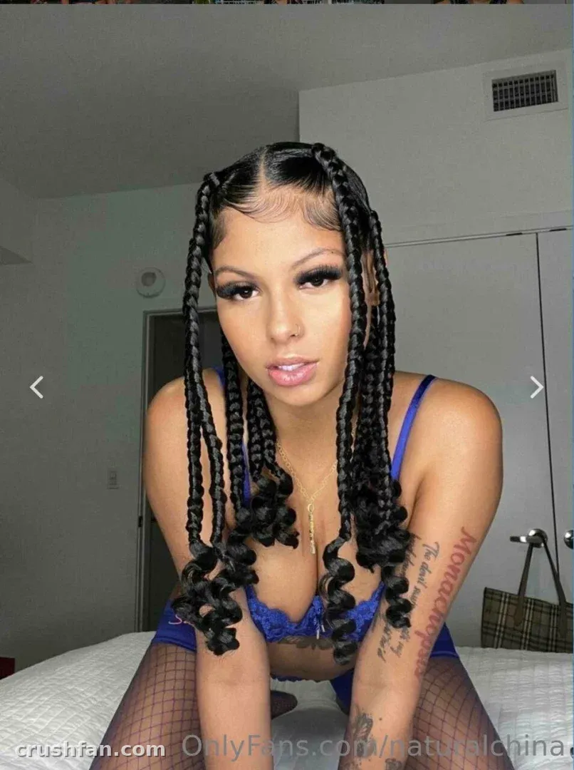 Creator with long braids and a blue lace top posing indoors in a close portrait.