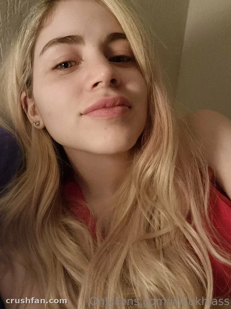 Willokhlass macht drinnen ein Nahaufnahme-Selfie mit langem blonden Haar und einem roten Oberteil.