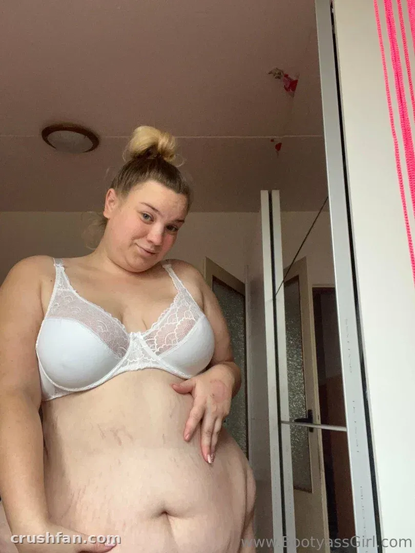 Bootyass Girl в белом кружевном бюстгальтере стоит рядом с зеркалом в помещении
