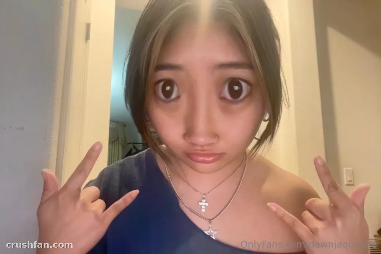 Close-up selfie of Dawn Jaqueline in a blue top, making a playful face with both hands raised