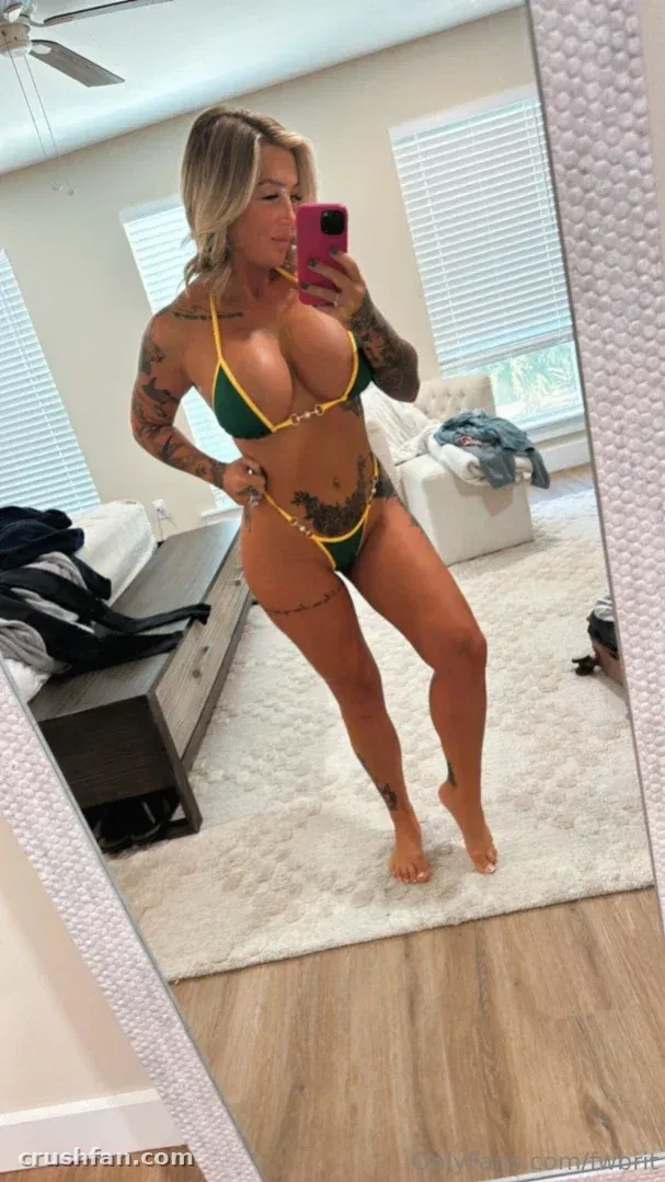 Britt de biquíni verde e dourado tirando uma selfie no espelho em um quarto claro