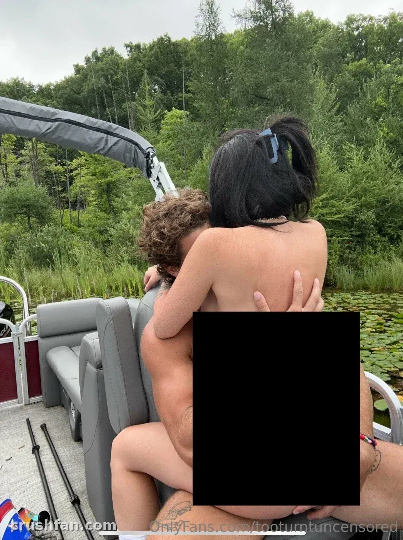 Too Turnt Tony sur un bateau avec une accompagnante en bikini, entouré d'arbres et d'eau.