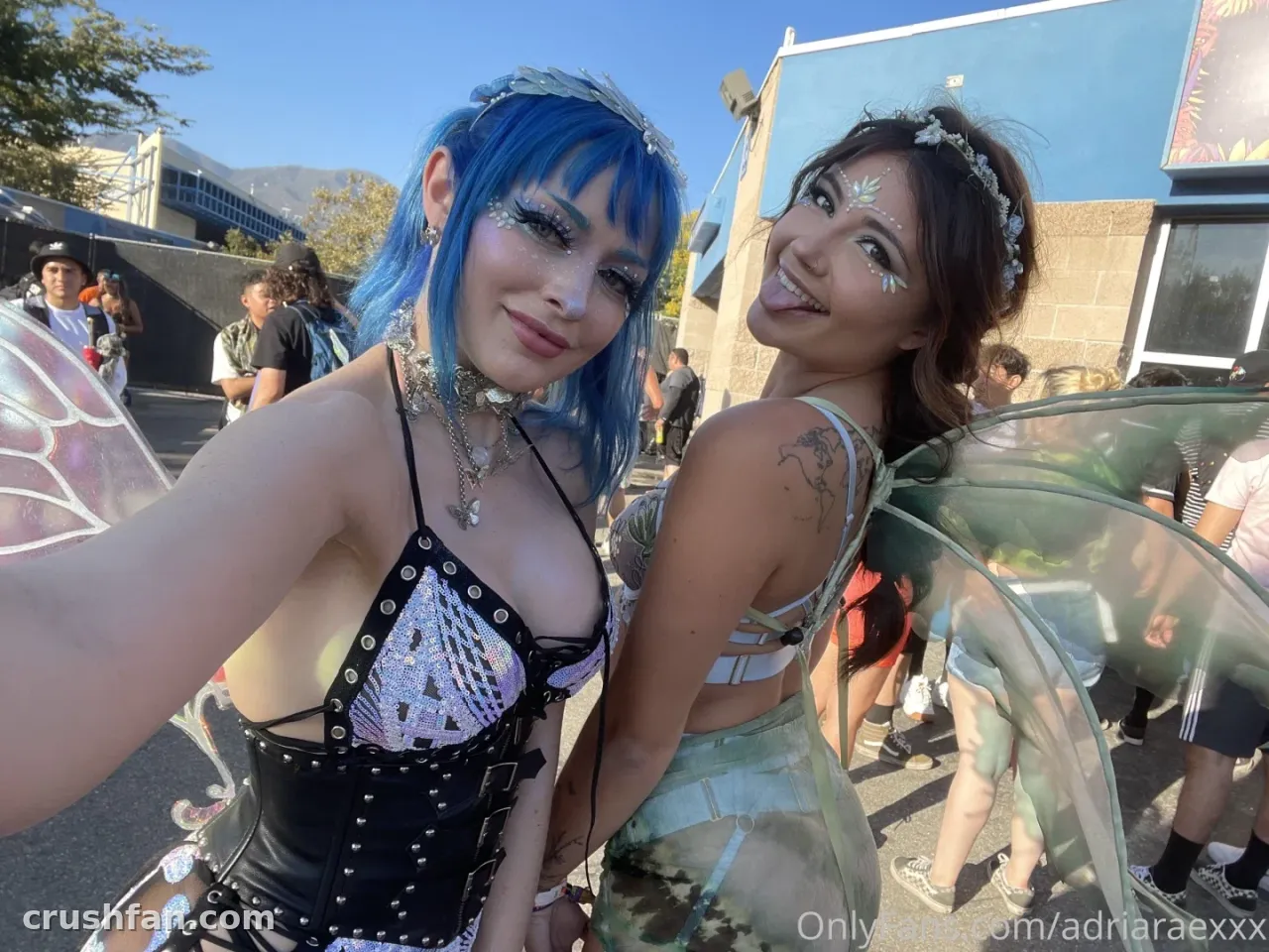 Creadora con pelo azul y alas de hada sonriendo en una selfie al aire libre en un evento diurno