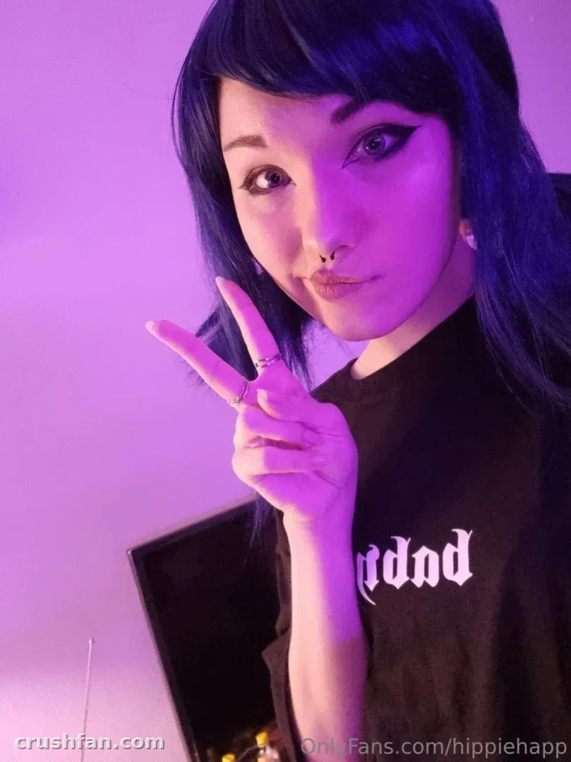 A criadora Happy sob luz roxa fazendo um sinal de paz enquanto veste uma camiseta gráfica preta