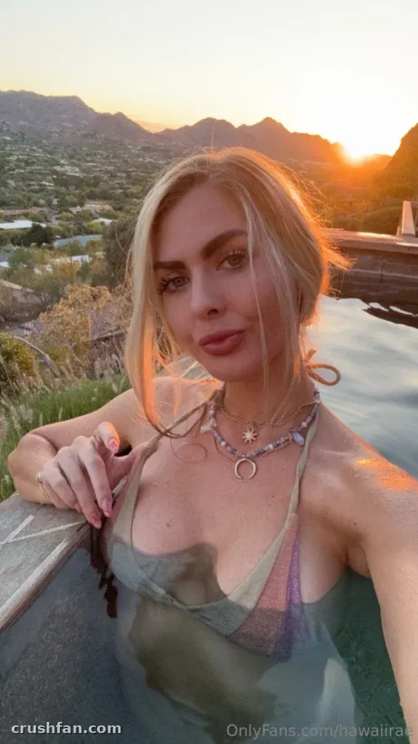 Hawaii Rae perto de uma piscina ao pôr do sol usando um top transparente e colares em camadas.